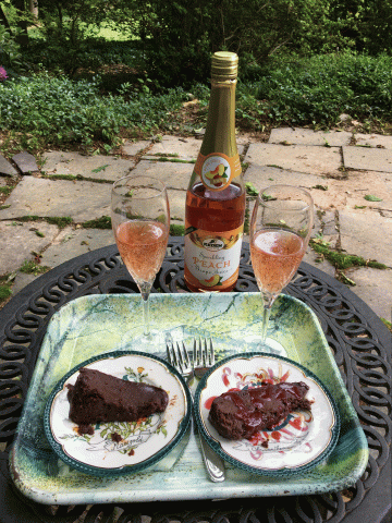 Two slices of Chocolate Cake on a tray, with glasses of peach juice behind the tray on a table.  Patio in the background.